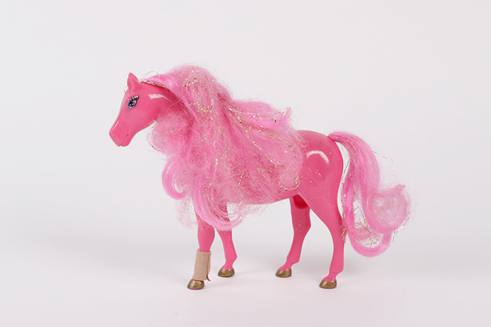 Zu sehen ist ein pinkes Spielzeug-Pferd mit einem Pflaster um ein Knöchel.