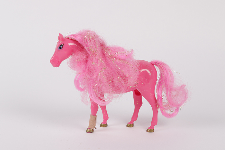 Zu sehen ist ein pinkes Spielzeugpferd mit goldenem Glitzer in der Mähne und goldenen Hufen. 